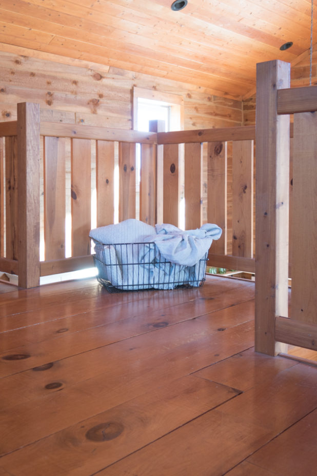 Wire Basket Filled With Linens and Ticking On The Landing of a Log Home